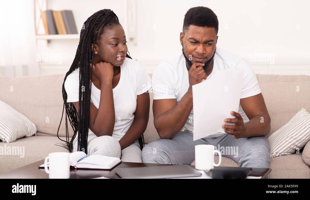 Black married couple reading papers sitting on couch at home, checking bills or insurance agreement, panorama Stock Photo