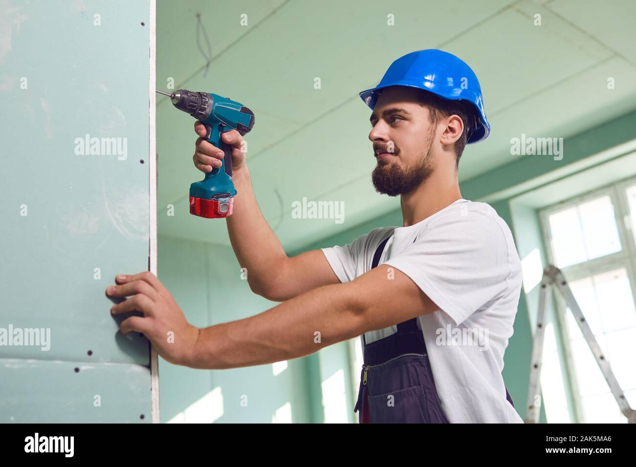 Worker builder installs plasterboard drywall at a construction site office open space. Plasterboard installer. Stock Photo