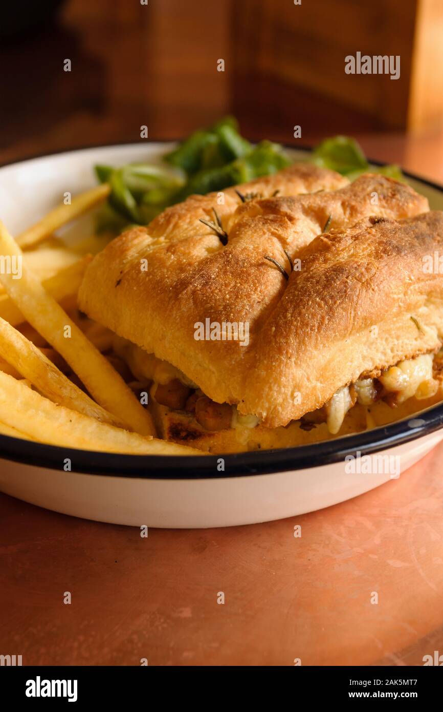 Grilled Focaccia bread sandwich filled with melted cheese sausage and served with French fries and salad Stock Photo