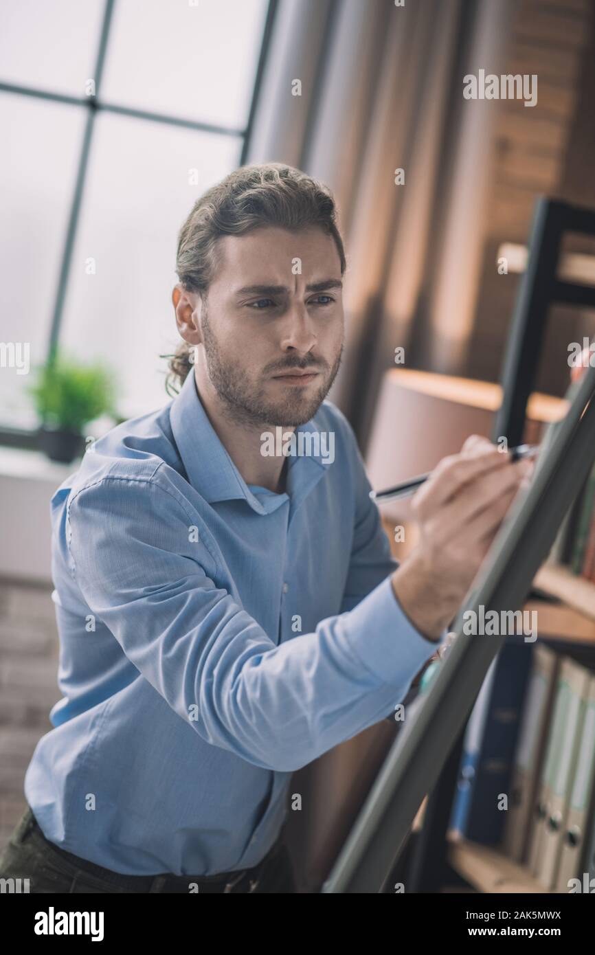 Making schemes. Young bearded man in eyeglasses writing on white board Stock Photo