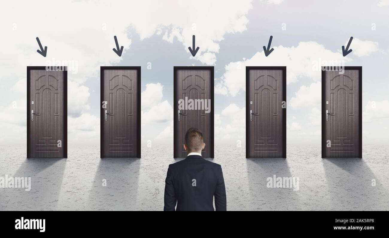 Choice concept. Rear view of businessman choosing the right door, each door indicated with arrow over sky background, panorama Stock Photo