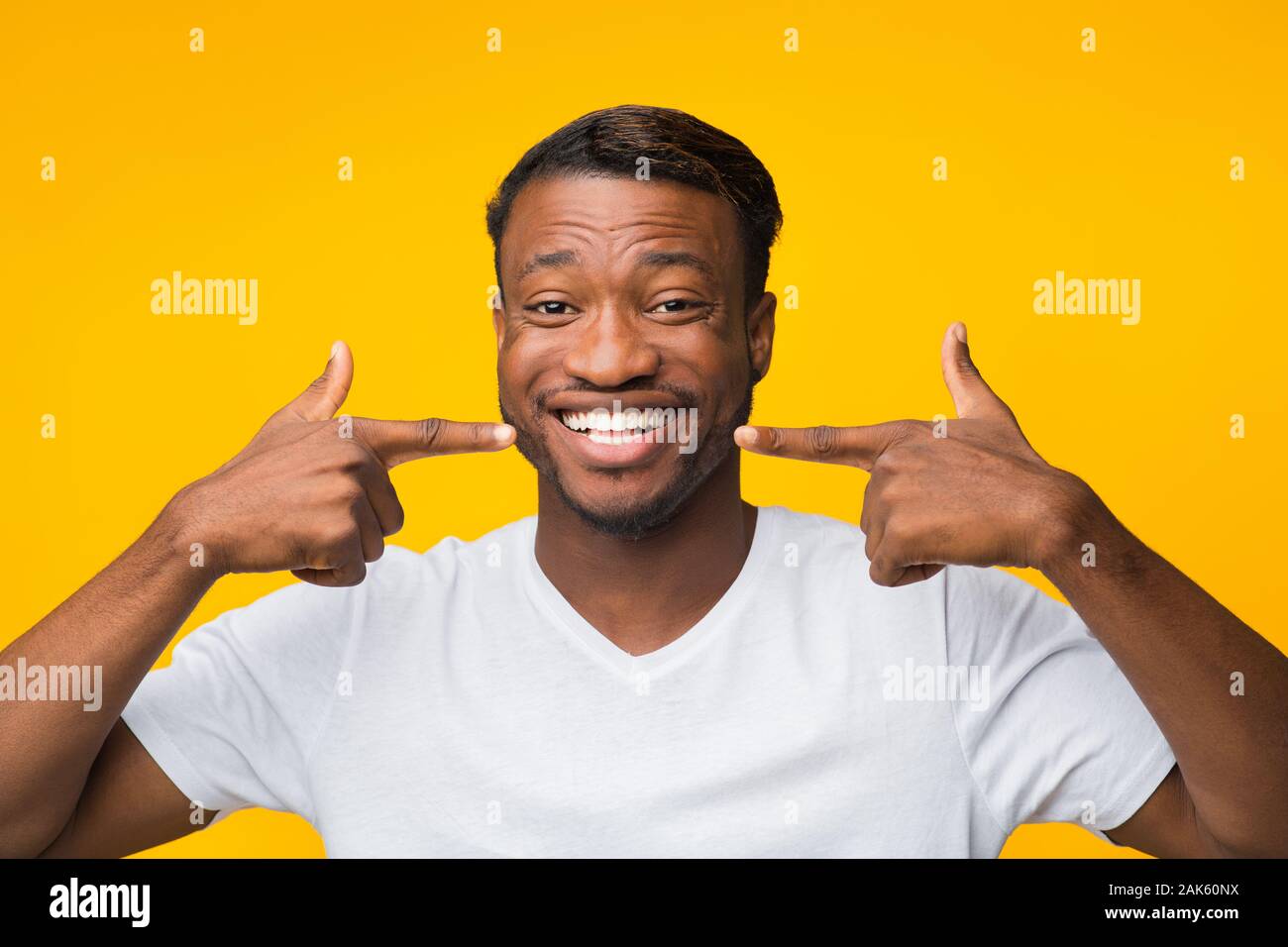 Joyful Afro Man Pointing Fingers At His Perfect White Smile Standing On Yellow Background. Studio Shot Stock Photo