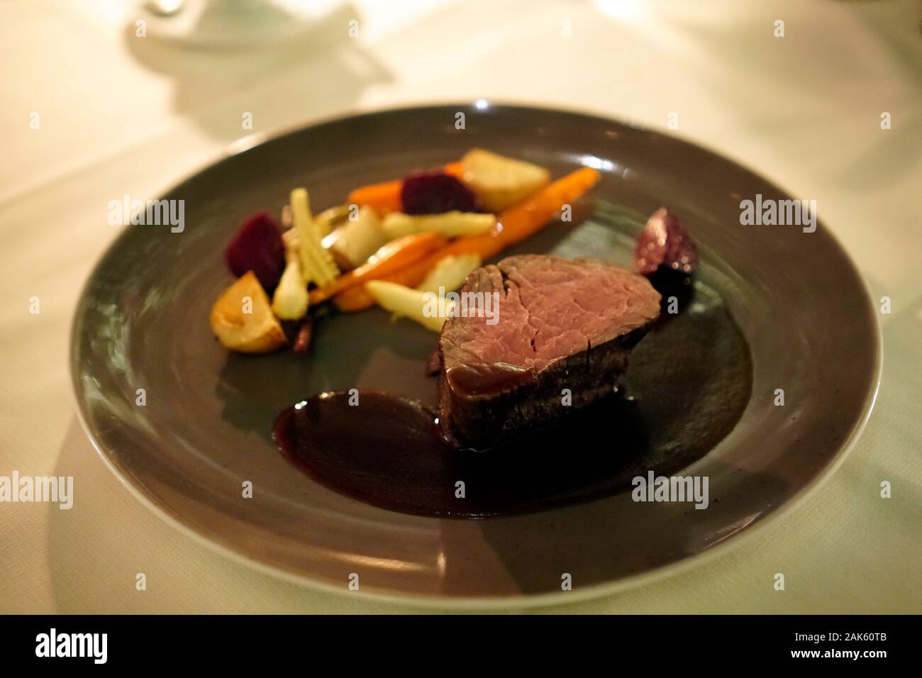 Stake - rare made with different vegetables and a dark brown sauce on the dark brown green color plate. Stock Photo