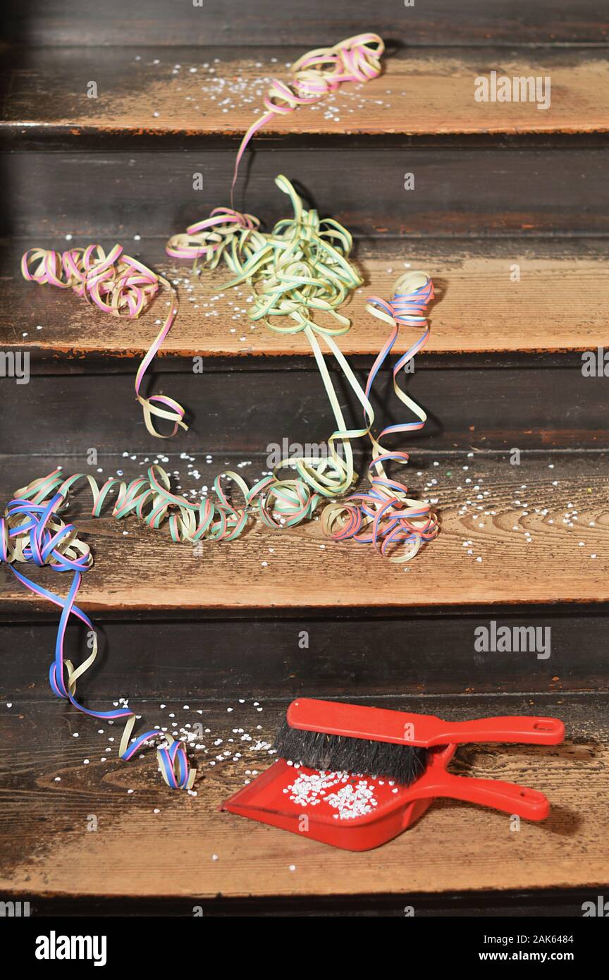 confetti and ribbons on wood steps and a broom with a dust pan - cleaning up after the party Stock Photo