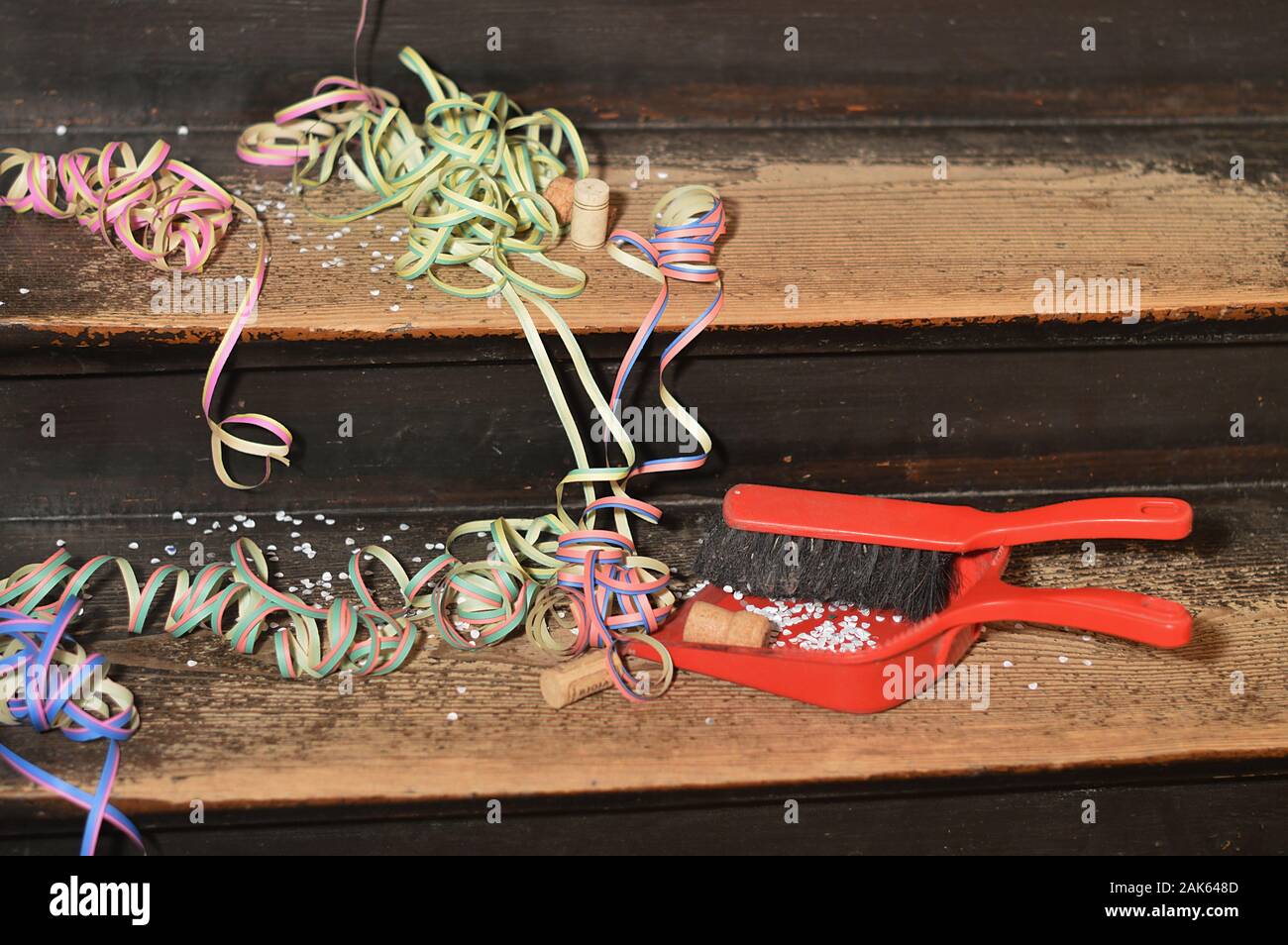 confetti and ribbons on wood steps and a broom with a dust pan - cleaning up after the party Stock Photo