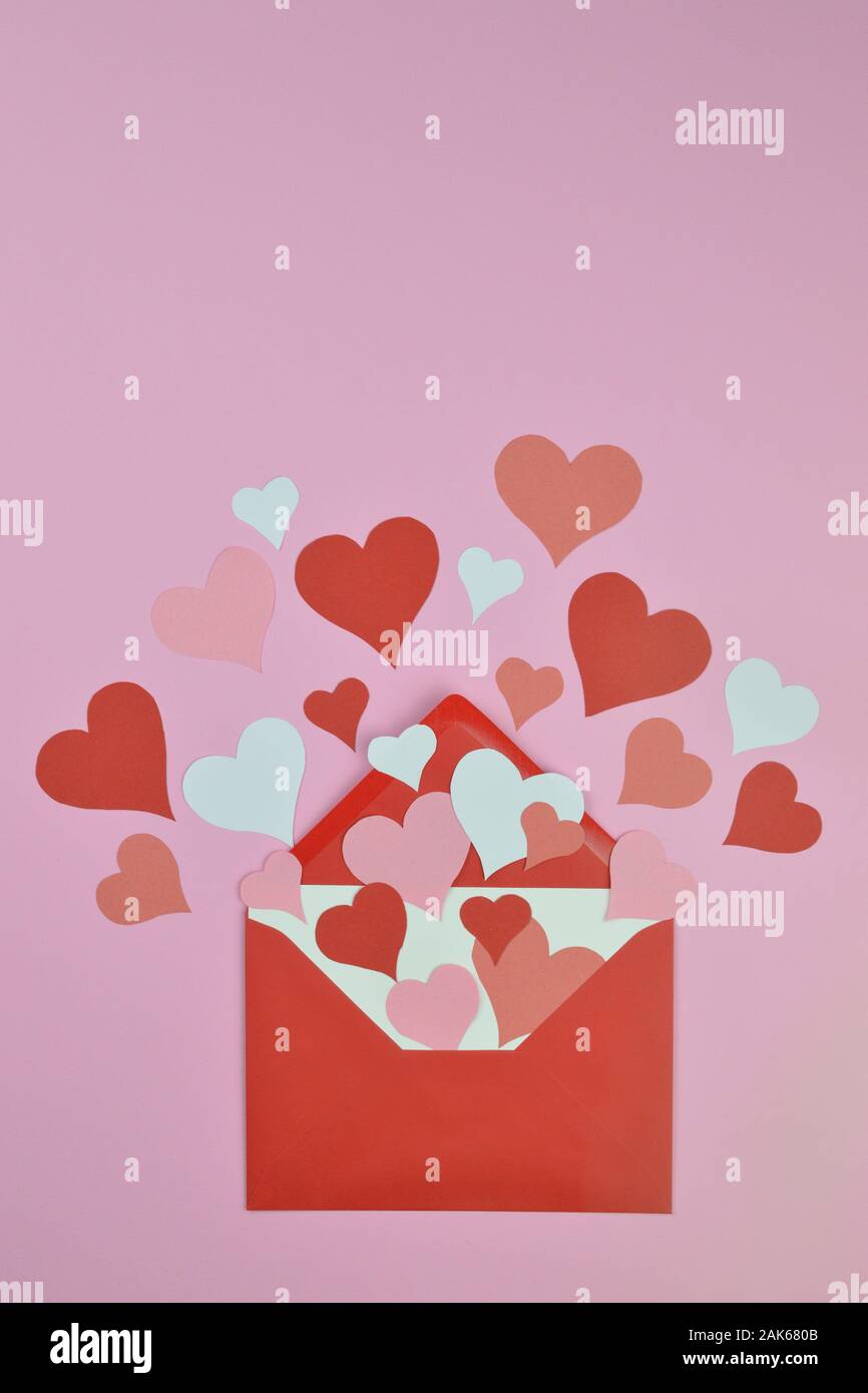 white blank letter in open red envelope with lots of different red, pink and white paper hearts coming out spread over pink background as love letter Stock Photo