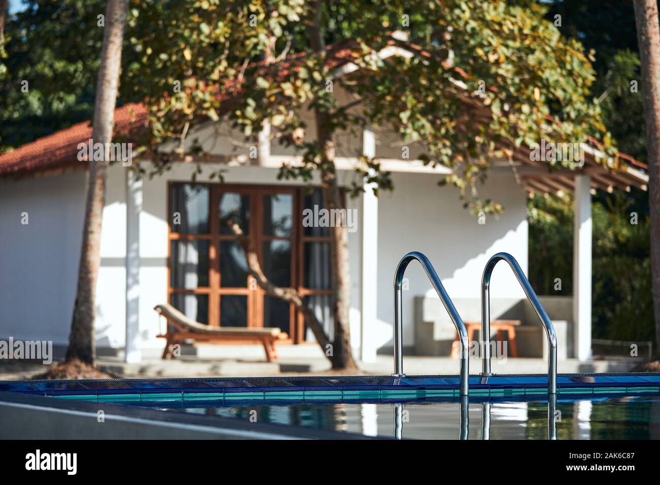 Luxury accommodation in tropical destination. Ladder to swimming pool against modern bungalow. Stock Photo
