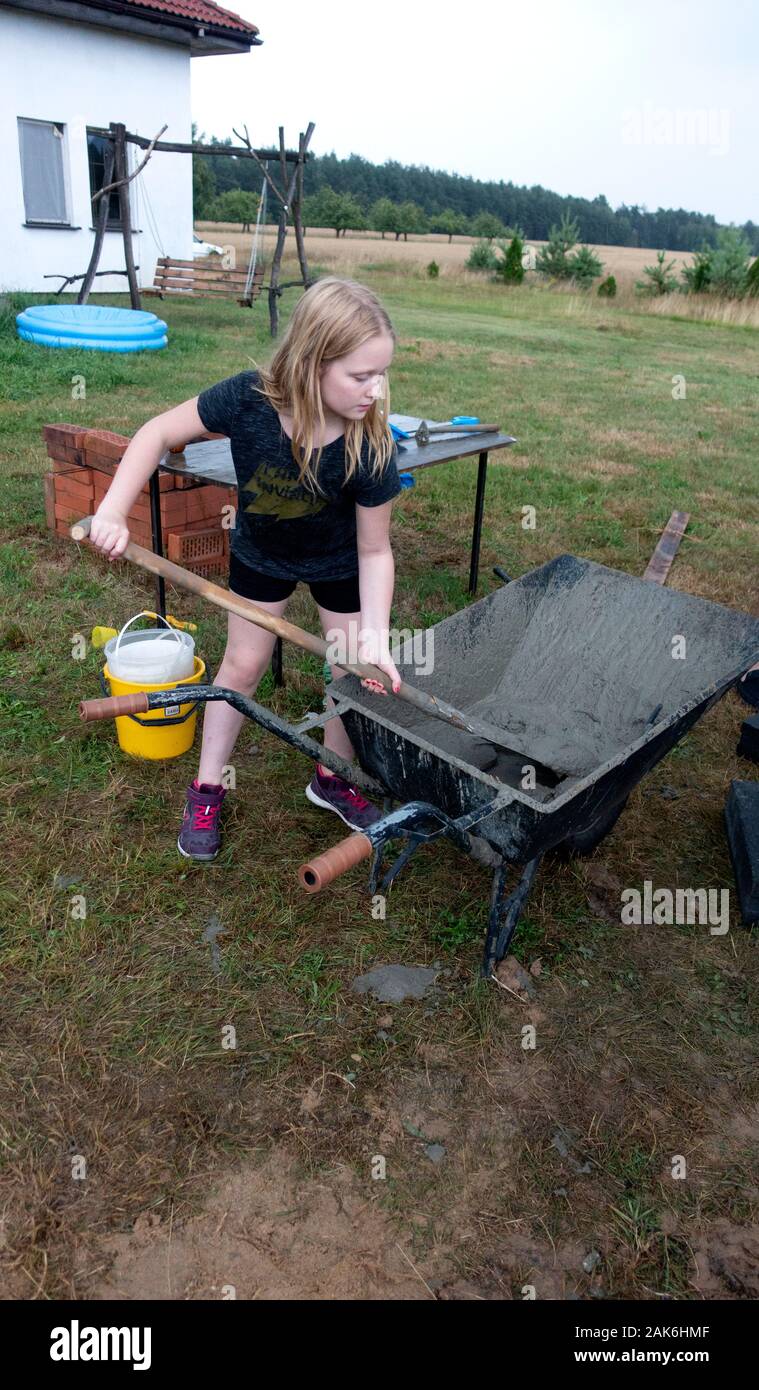 Hard working young girl age 11 mixing cement for building an outdoor family fireplace. Zawady Gmina Rzeczyca Poland Stock Photo