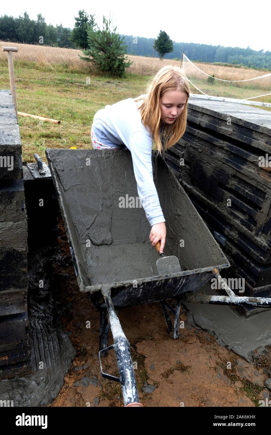 Preteen Girl Scrapping Last Bit Of Cement From Wheelbarrow With