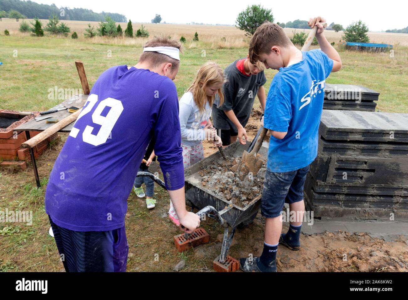 Cousins Working Together Mixing Cement In Wheelbarrow For Making