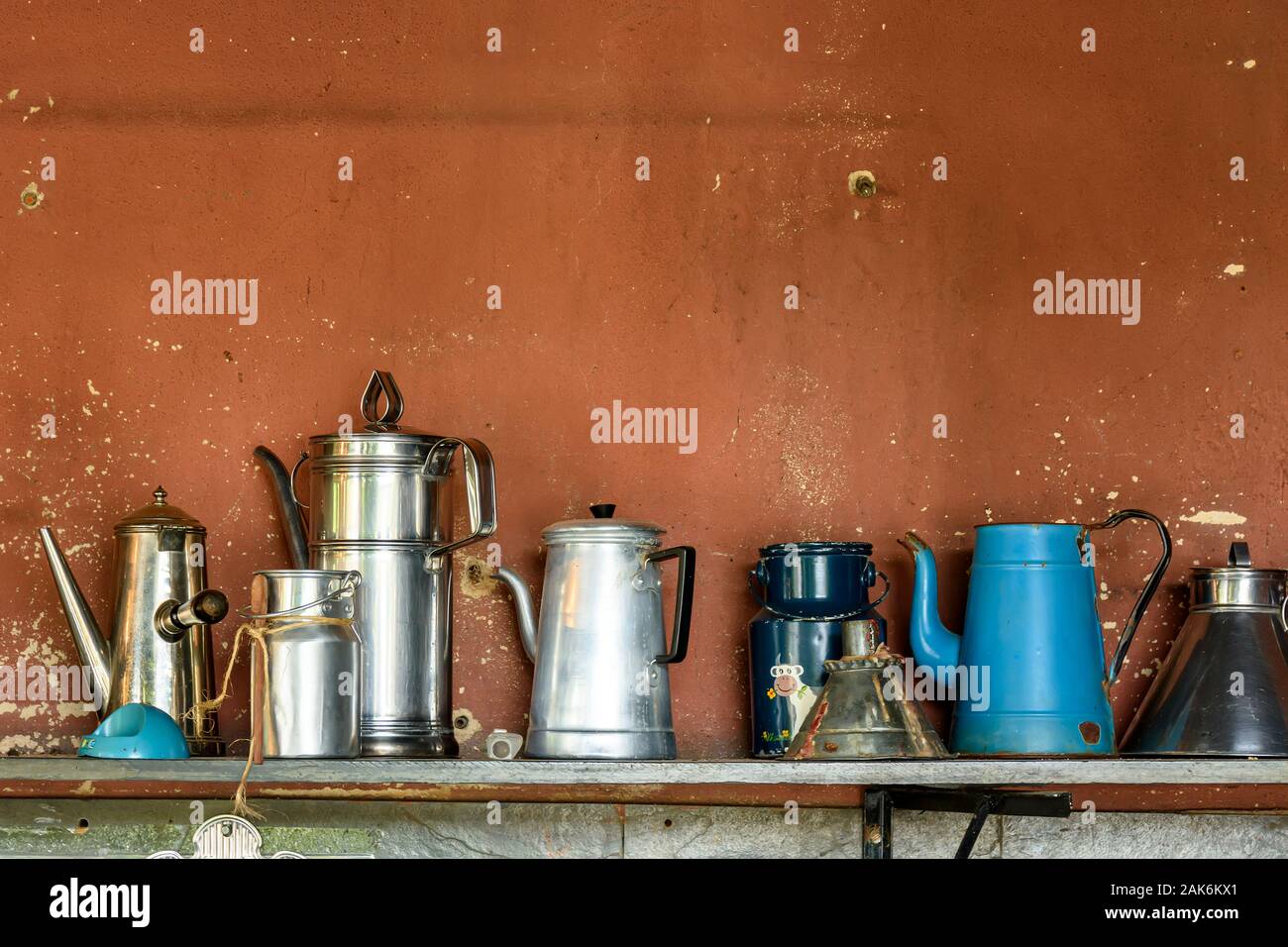 Collection of old and used coffee pots arranged on wooden shelf with rustic wall behind Stock