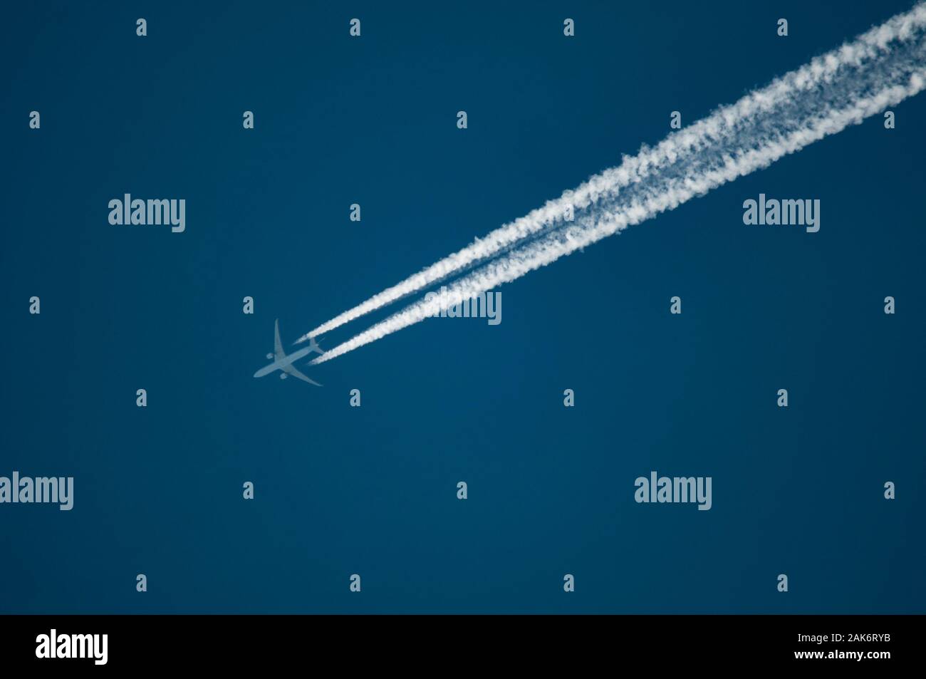 Contrails from a commercial jetlines at altitude flying diagonally across the frame in a clear blue and cloudless sky showing impact of jet travel Stock Photo