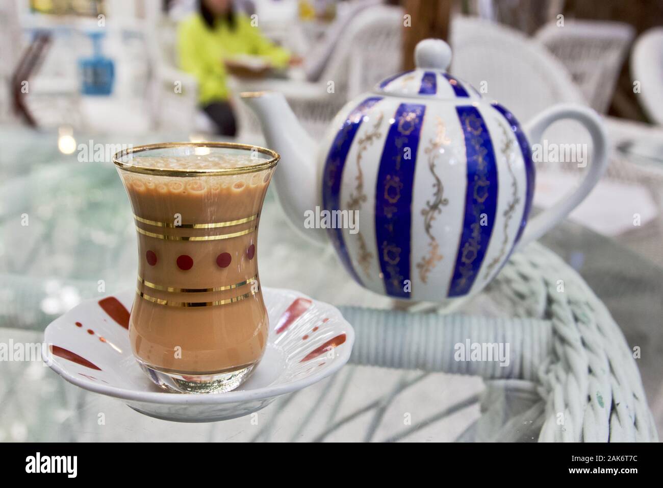 A glass of Karak Tea next to a striped teapot in Dubai, UAE Stock Photo