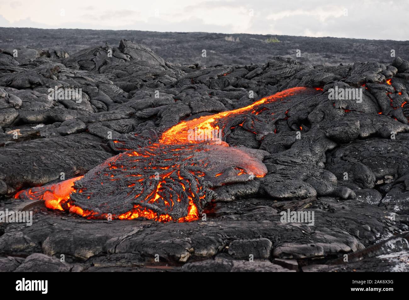 Hot magma of an active lava flow emerges from a fissure, the heat of the glowing lava makes the air flicker, the lava cools down slowly and solidifies Stock Photo