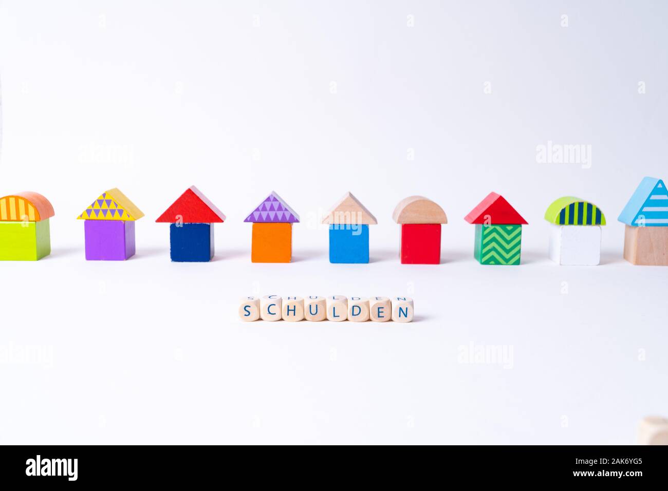 Cubes with letters saying 'Schulden', the German word for debt in front of a row of houses built of toy colorful toy blocks Stock Photo