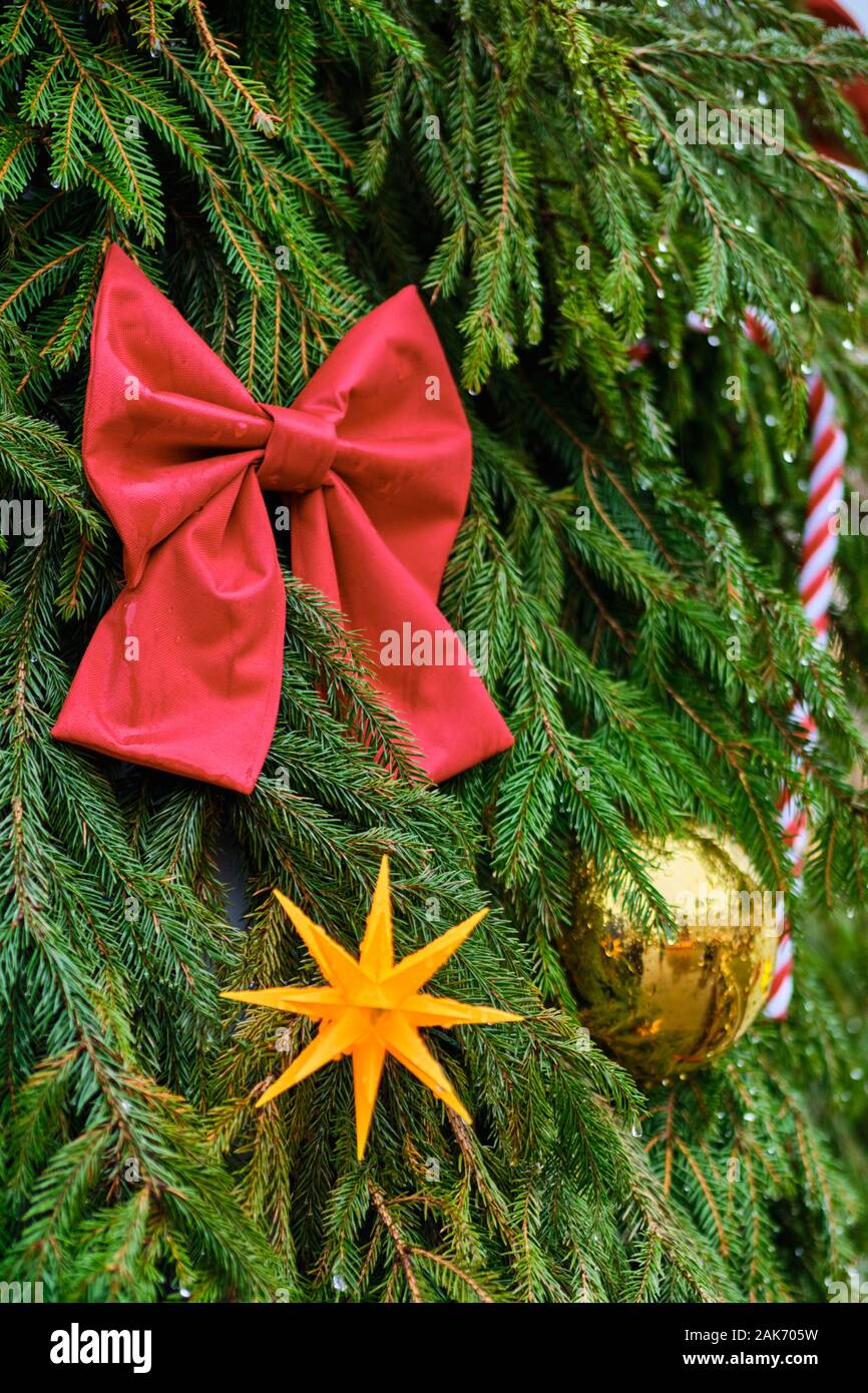 Christmas decoration in the form of a red bow with a yellow ball on a green christmas tree with a blurred background and bokeh. Close up. Vertical. Stock Photo
