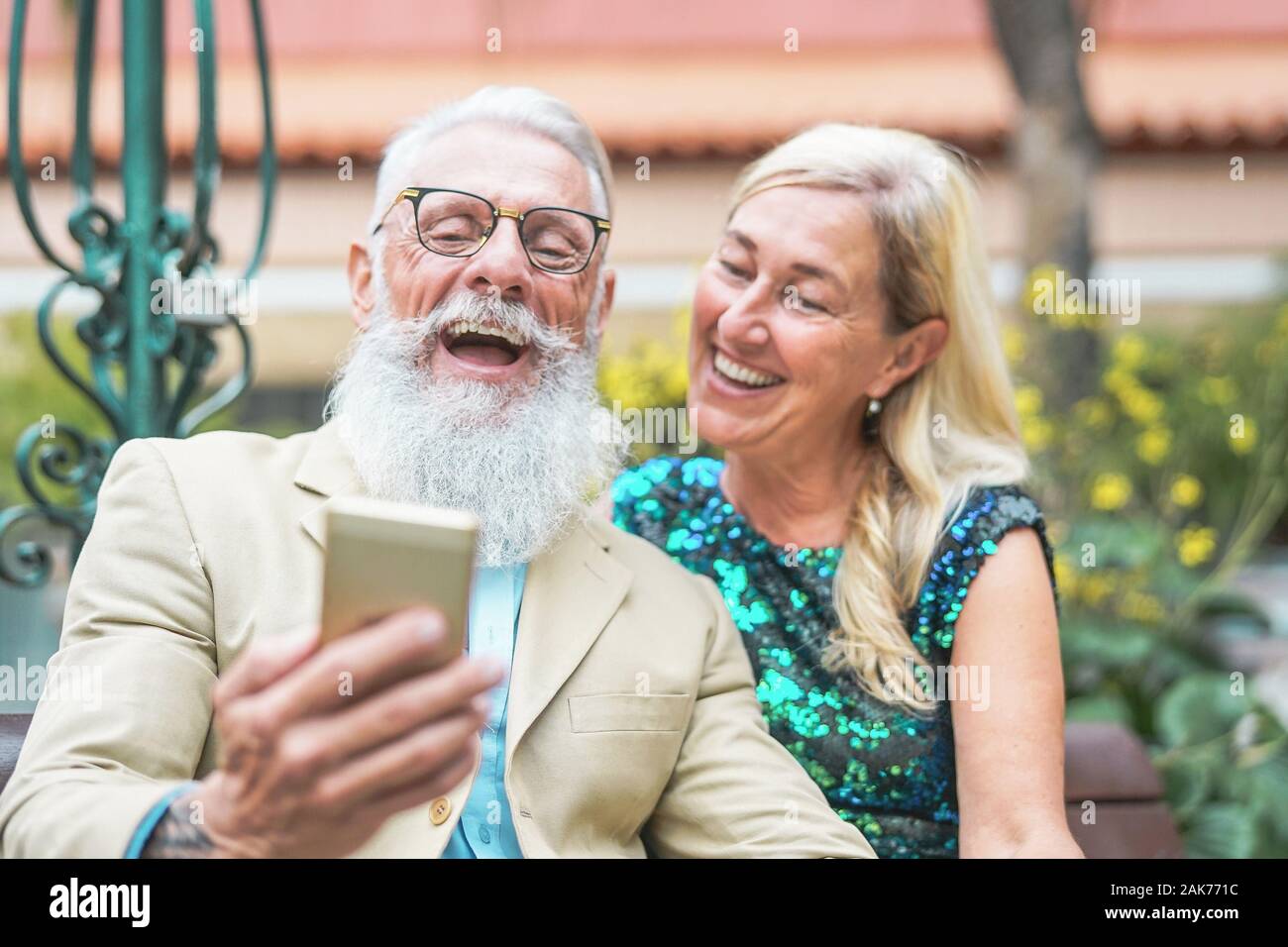 Happy senior couple watching on mobile smart phone and laughing together - Mature fashion people having fun with new technology cellphones outdoor Stock Photo