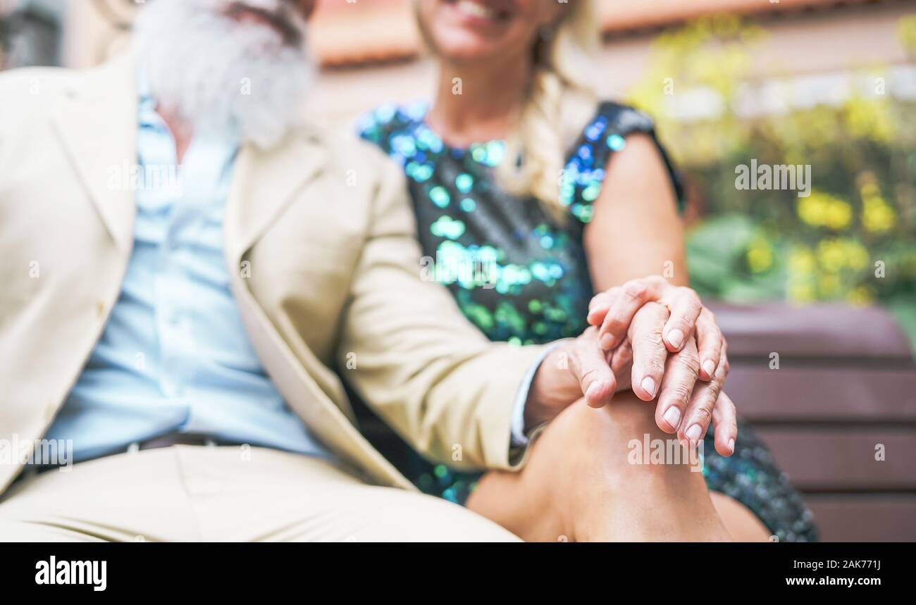 Happy senior couple having a romantic moment outdoor - Mature elegant people spending time together sitting on bench Stock Photo