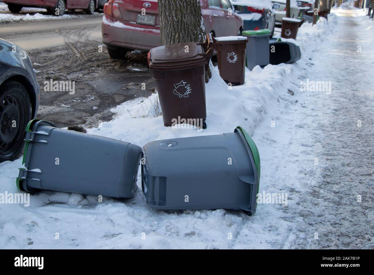 Recycling and compost bins on snowy sidewalk along street and cars in