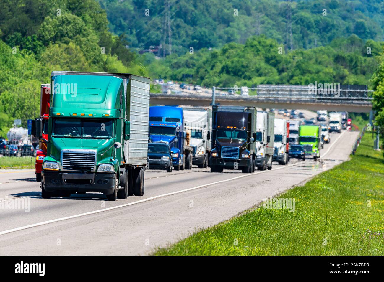 Horizontal shot of a green 18-wheeler leading the way in heavy traffic on an interstate highway. Stock Photo