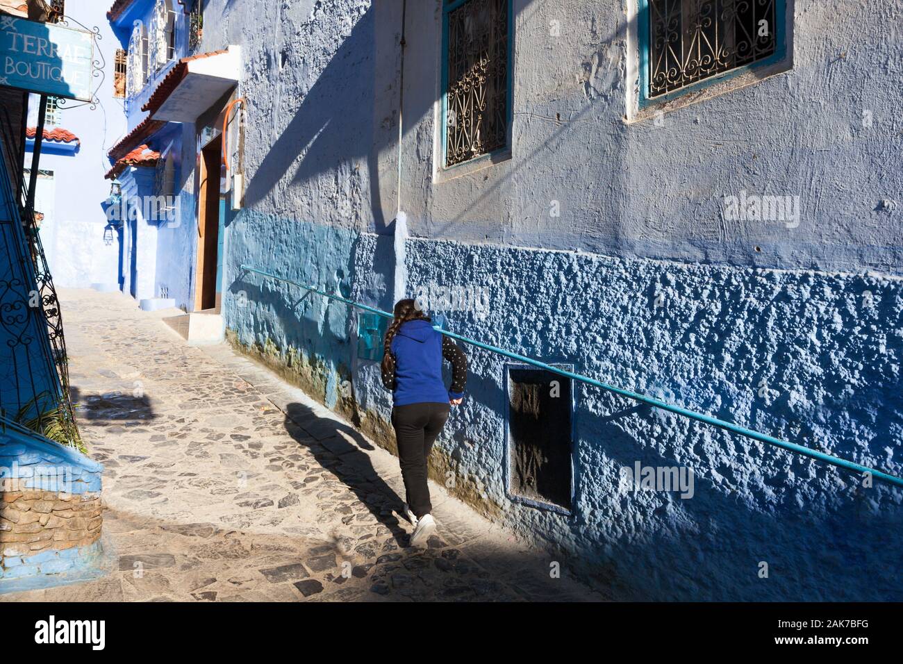A girl with braid and her shadow in the sunlit street of medina of Chefchaouen (also known as Chaouen), Morocco Stock Photo