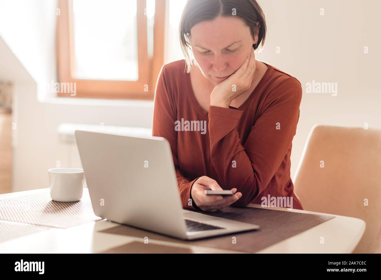 Woman telecommuting in home office interior. Portrait of female freelancer using mobile phone, selective focus. Stock Photo