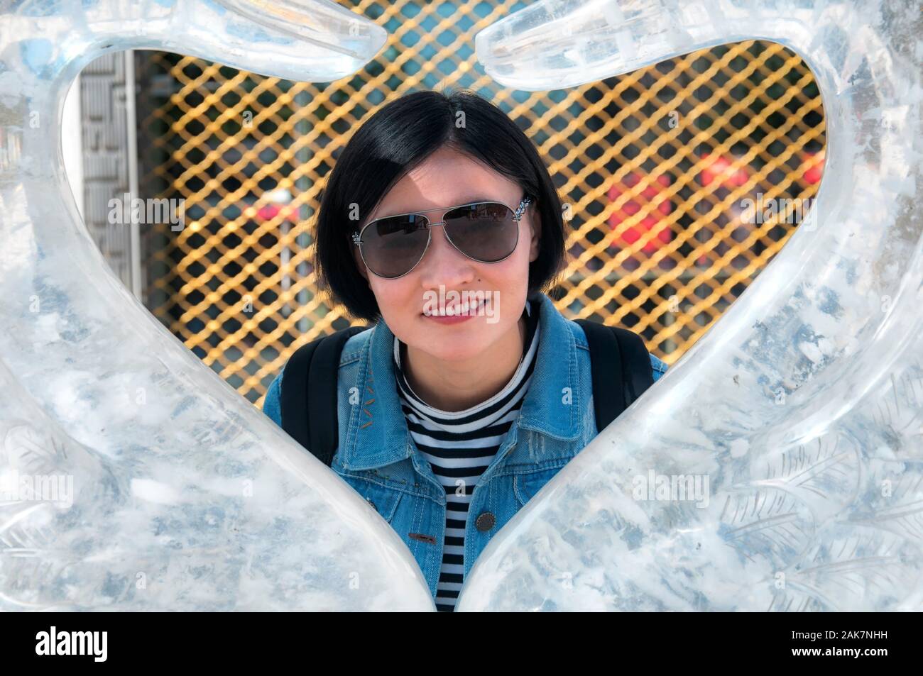 A happy chinese woman posing inside an ice swan sculpture heart in the city of harbin china on a sunny day. Stock Photo