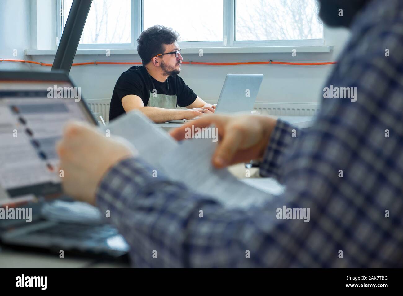 Young office worker looking outside, unable to concentrate on work, needing rest, boredom, need additional motivation Young office worker ponders over work task in his workplace Stock Photo