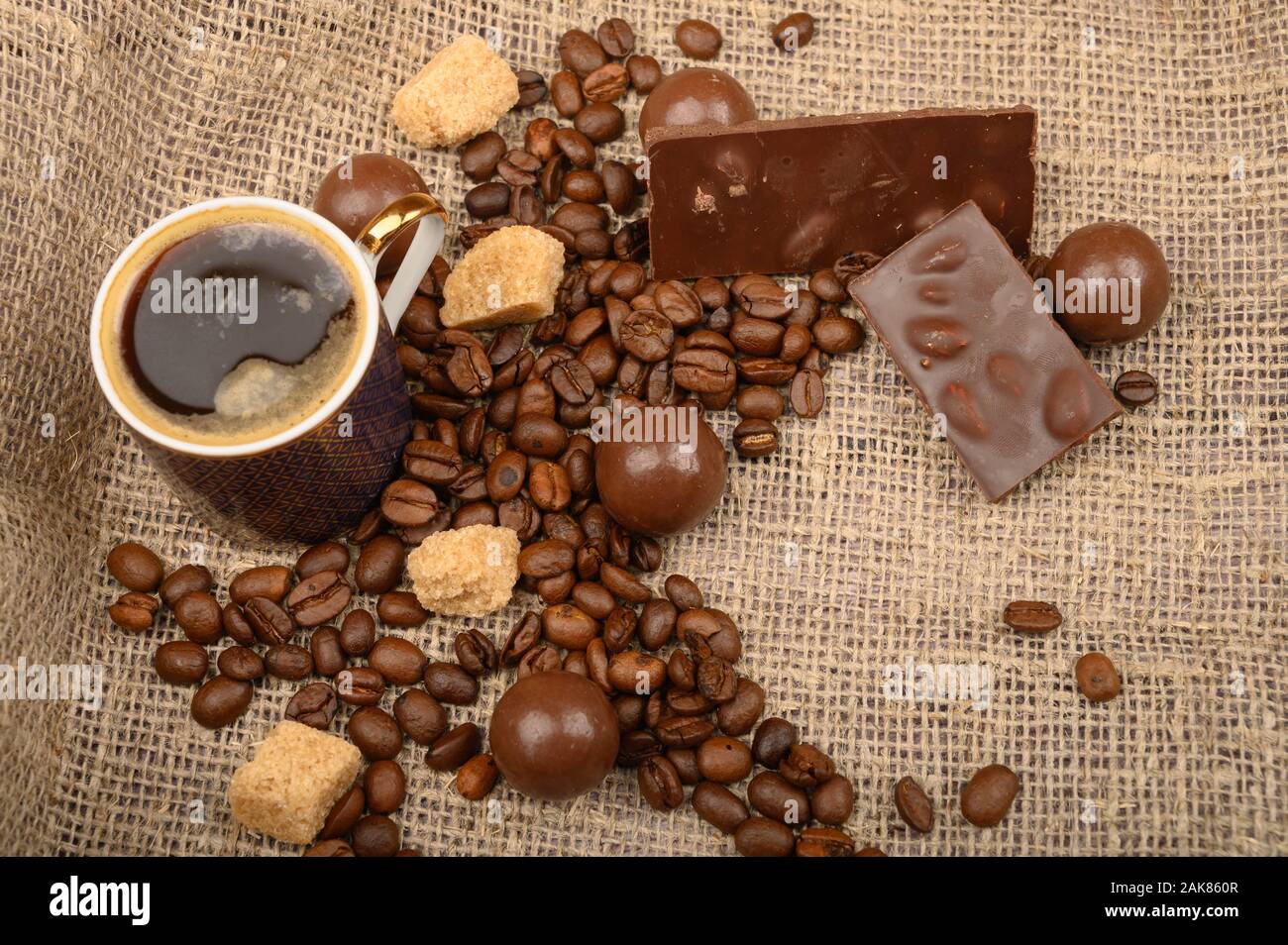 https://c8.alamy.com/comp/2AK860R/a-cup-of-coffee-coffee-beans-pieces-of-brown-sugar-and-chocolate-on-a-background-of-rough-homespun-fabric-close-up-2AK860R.jpg