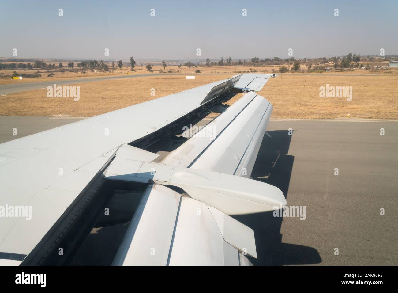 view of the open flaps, aileron and spoiler on a plane wing as it lands on a runway in Lanseria South Africa Stock Photo