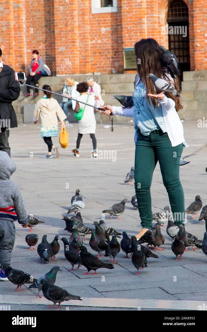 A woman feeding pigeons and posing for selfies in Piazza San Marco in Venice Italy Stock Photo