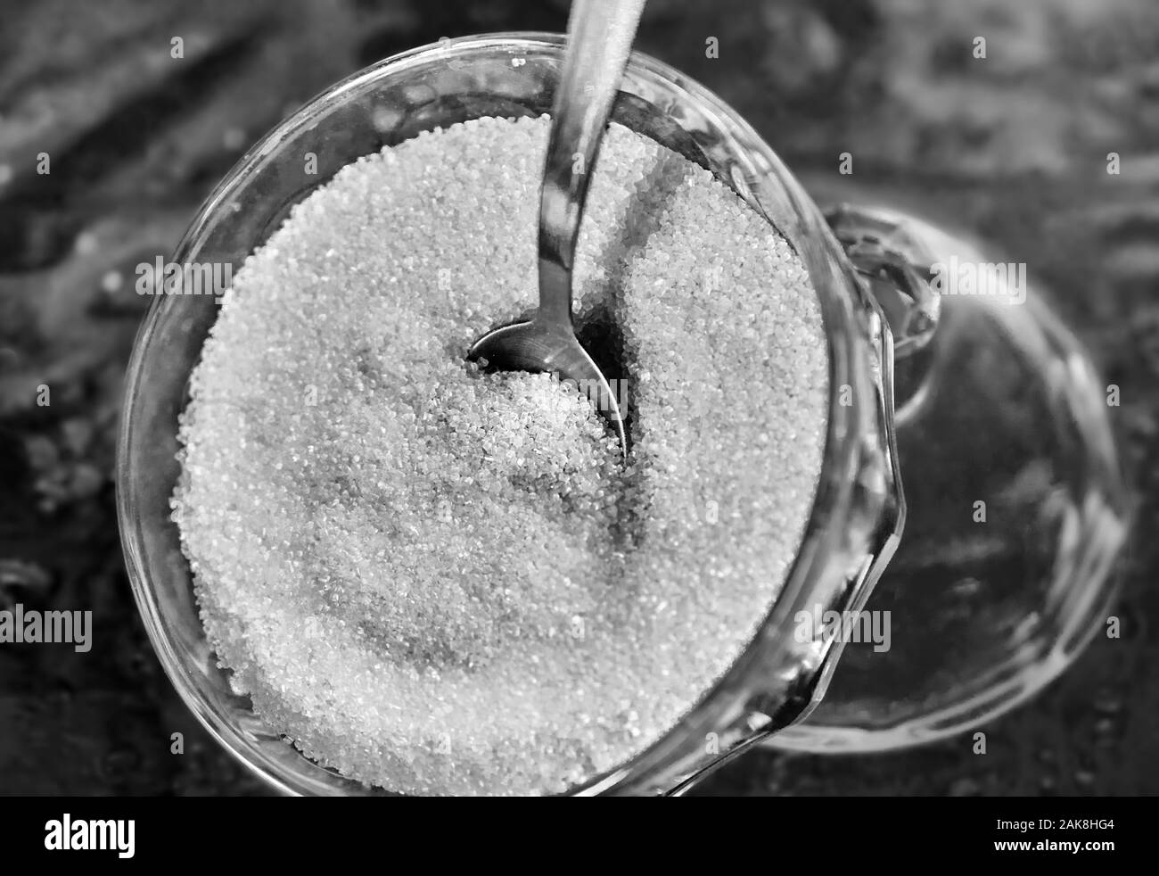 Glass bowl of granulated sugar with spoon on a glass table with a pattern Stock Photo