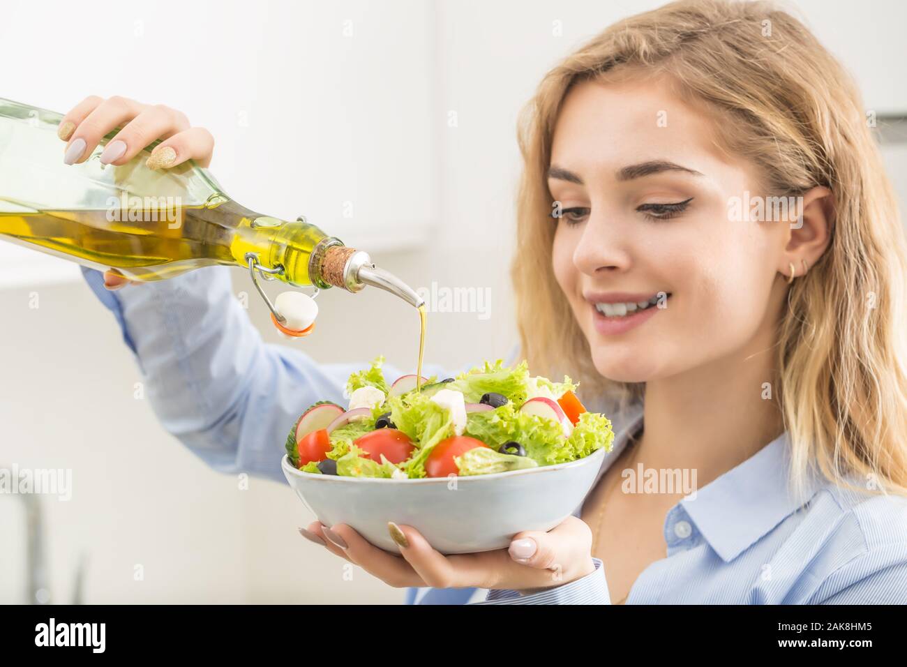 Young woman pouring olive oil in to the salad. Healthy lifestyle eating concept. Stock Photo