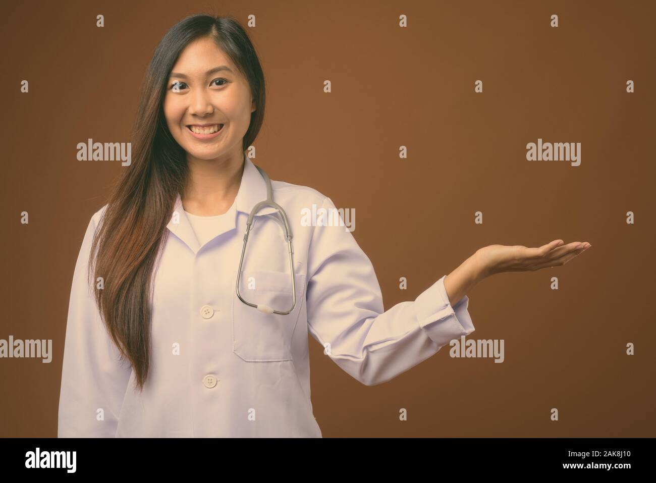 Young beautiful Asian woman doctor against brown background Stock Photo ...