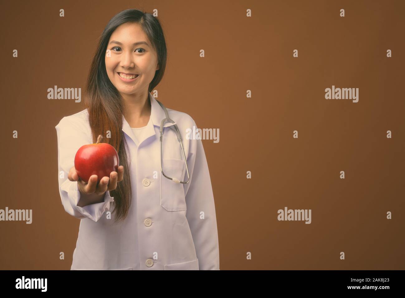 Young beautiful Asian woman doctor against brown background Stock Photo ...