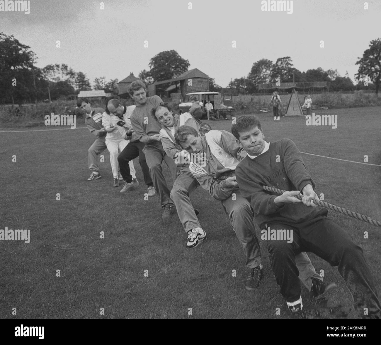 1980s, historical, a group of male adults in a field competing in a tug-of-war contest, all pulling together with effort on a rope, England, UK. Stock Photo