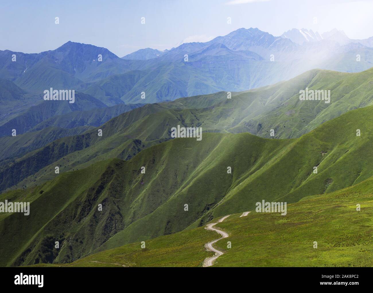 A majestic panorama of a rocky mountain range with forest-covered slopes of mountains in the foreground. A country road stretching into the distance Stock Photo