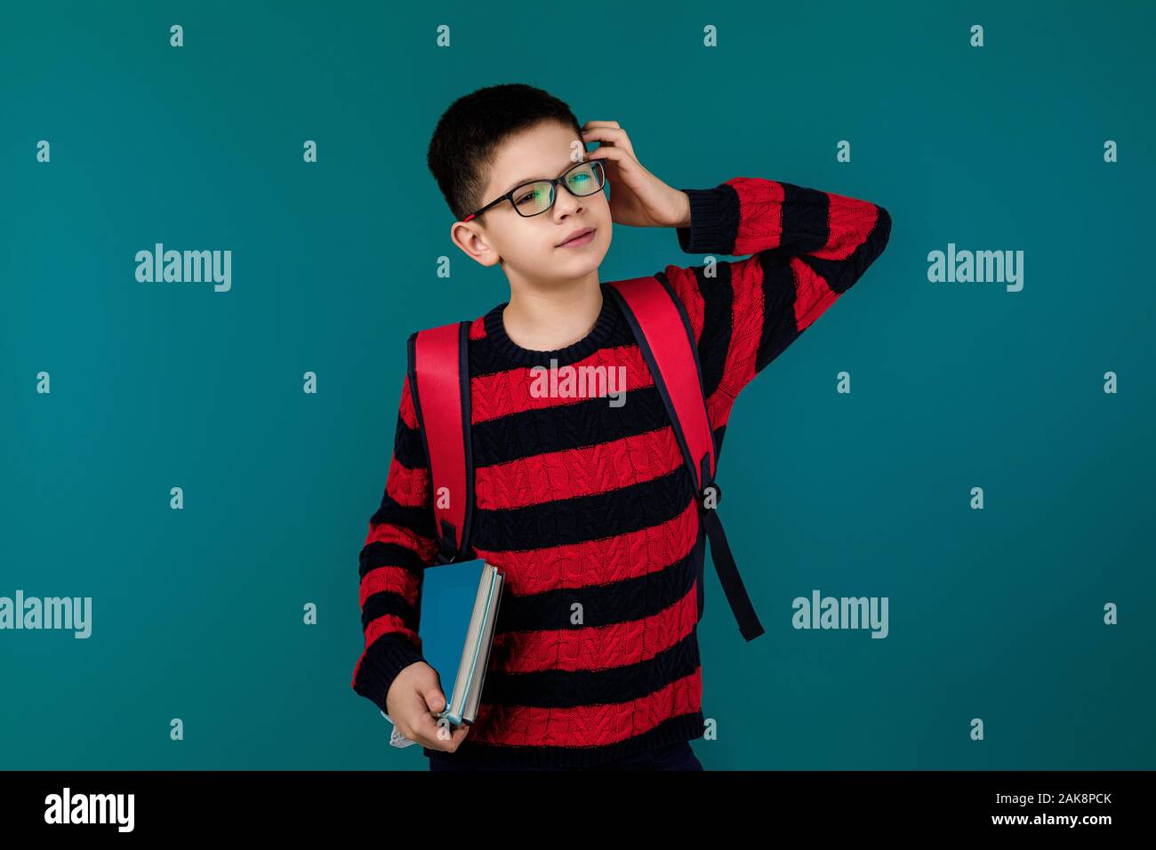 little cheerful school boy wearing glasses holding a book over blue ...