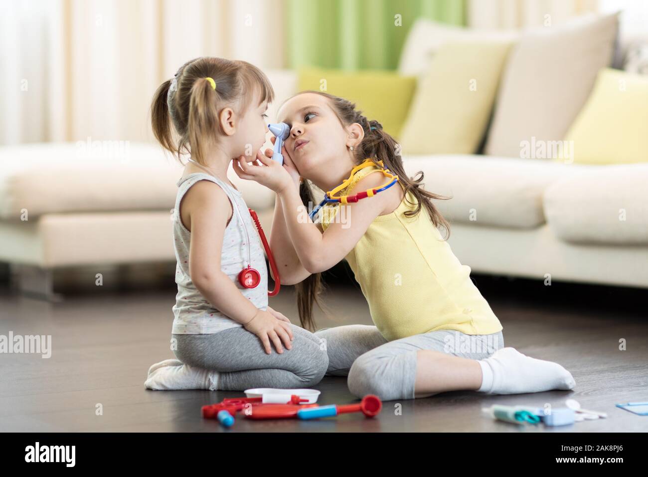 Child girl and toddler sister playing doctor with tools in living room Stock Photo