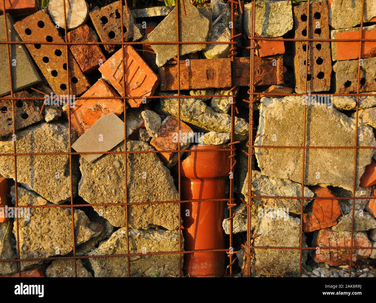 A hand made gabion wall in a suburban garden uses broken bricks and concrete and pipes from the site Stock Photo