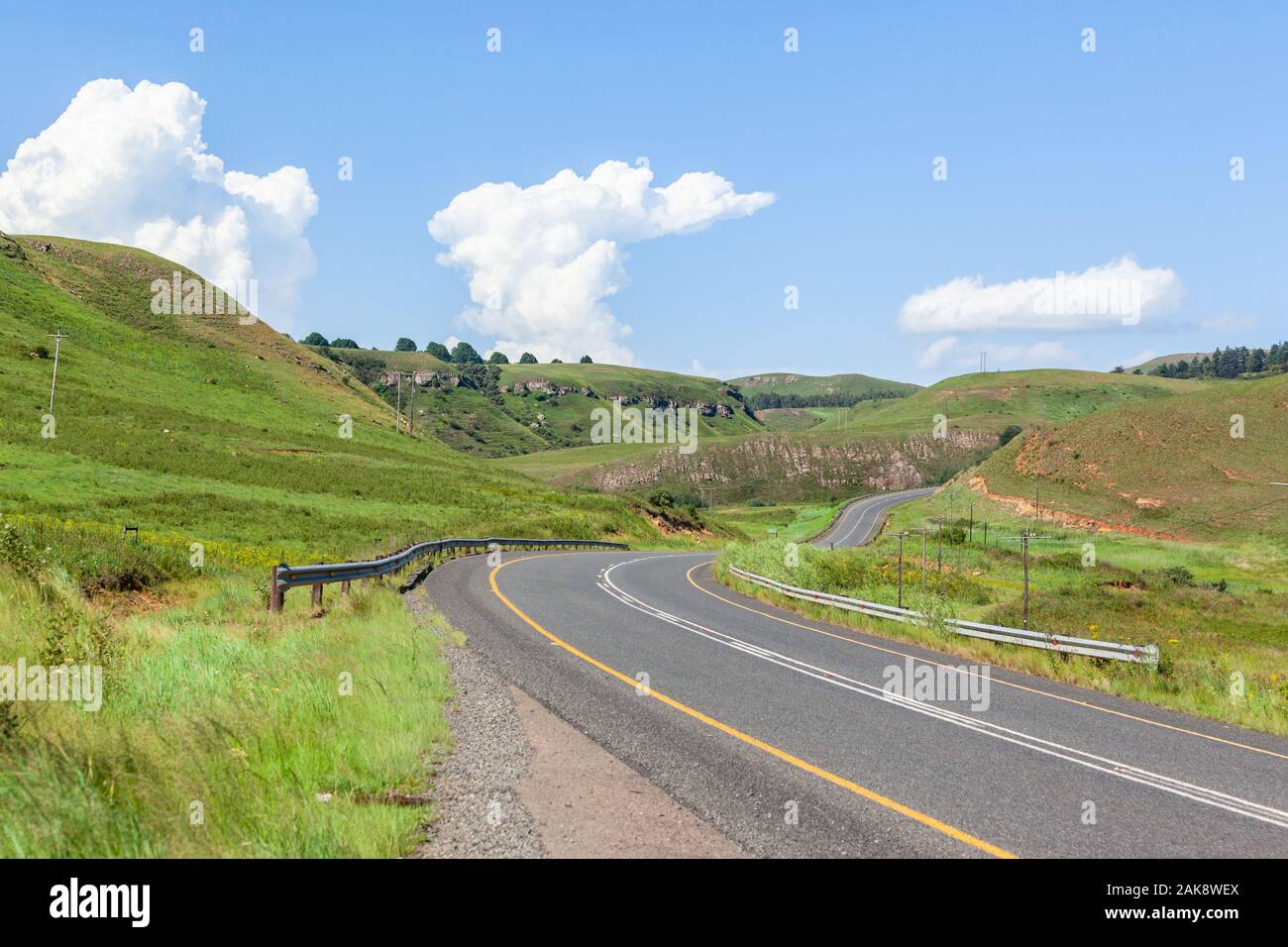 Scenic asphalt road travel route winding through valley and green hills blue sky clouds summer landscape. Stock Photo