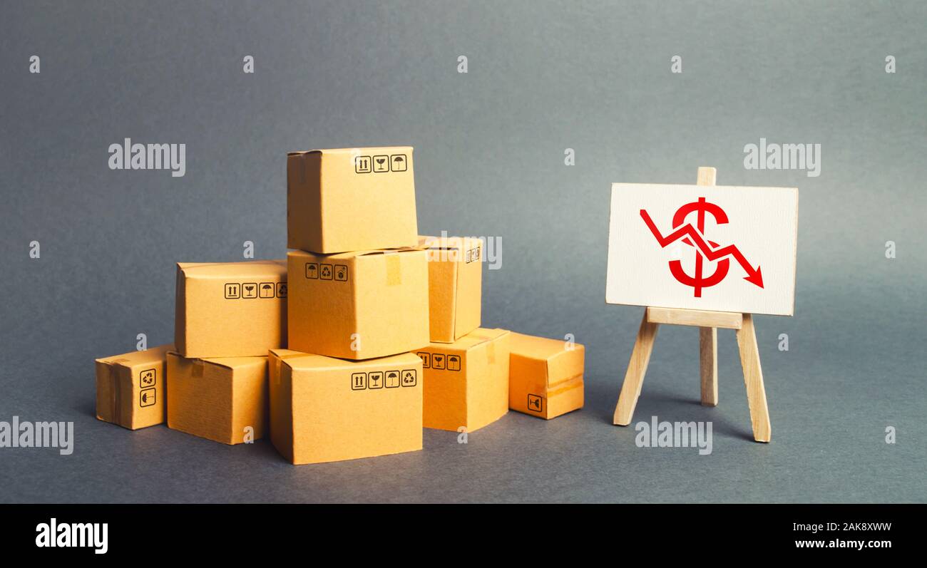 Pile of boxes and easel with dollar red arrow down graph chart. Drop in profits, slowdown in sales. Fall in imports or exports, trade deficit. Low pro Stock Photo