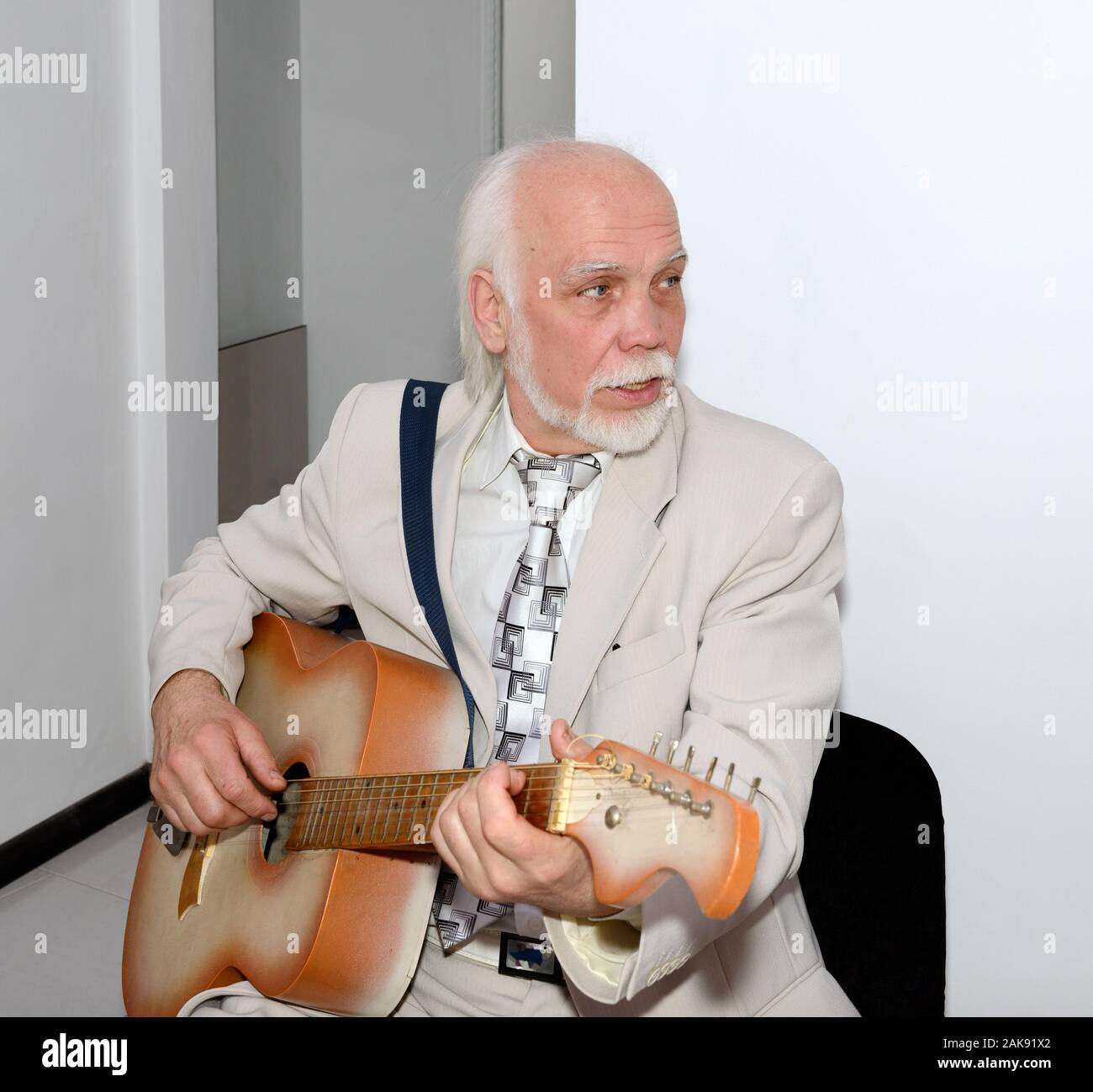 Portrait of senior grey bearded bald man in light business suit that is sitting with guitar in office interior. Stock Photo