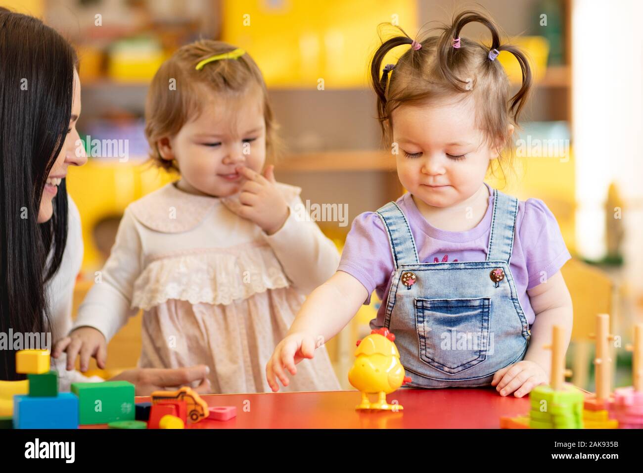 Babies group playing with teacher in day care centre nursery playroom Stock Photo