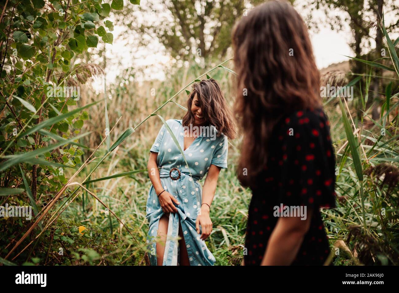 Two young women walking through the field the field wearing dresses and sneakers Stock Photo