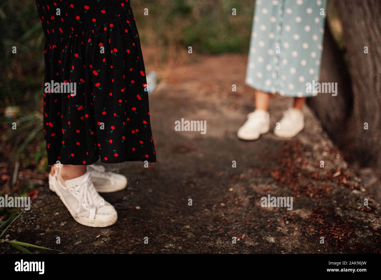 Lower view of two young women walking through the field the field wearing dresses and sneakers Stock Photo
