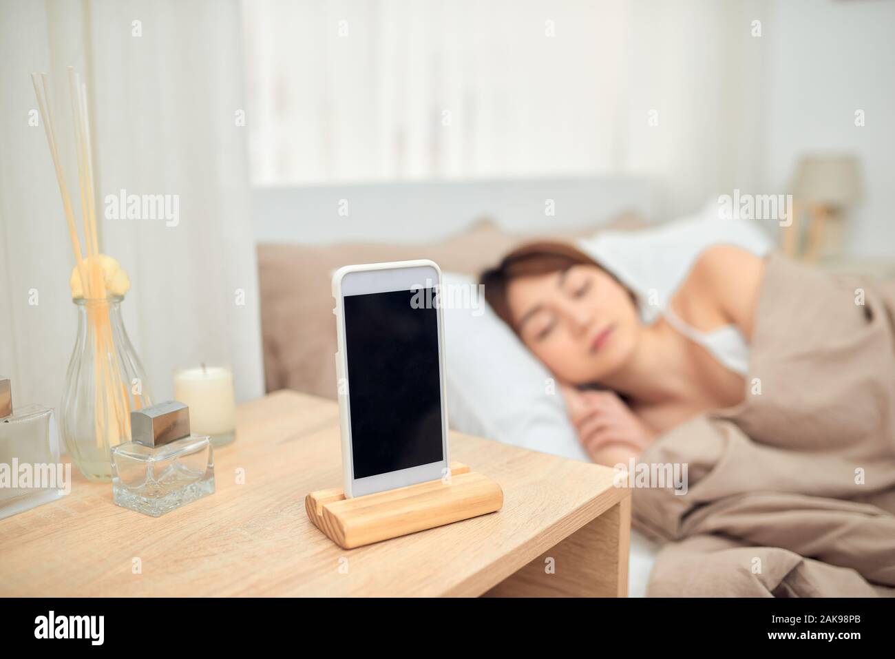 Asian Woman Asleep In Bed Woken By Alarm On Mobile Phone Stock Photo
