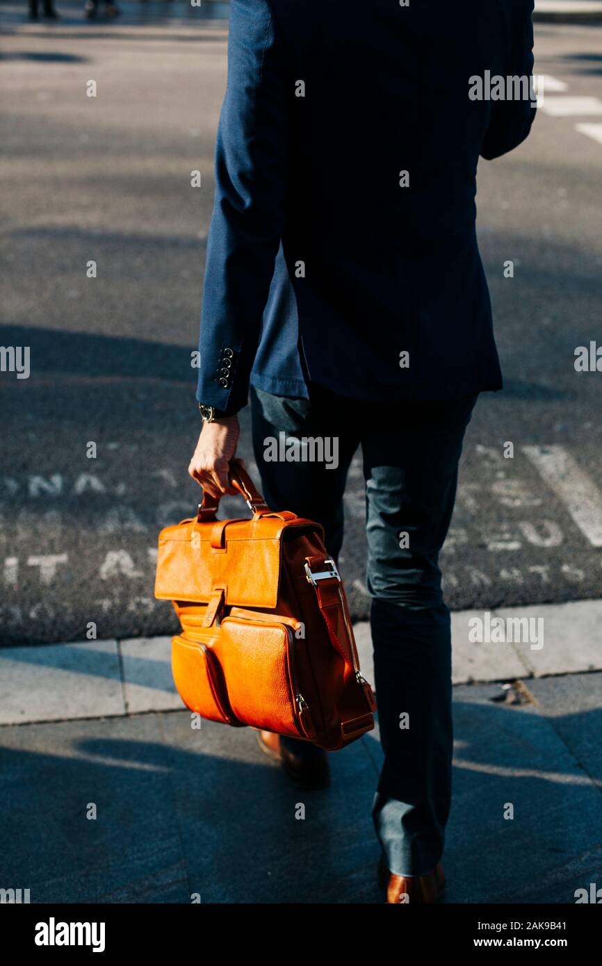 Executive man carrying a leather bag while walking down Passeig de