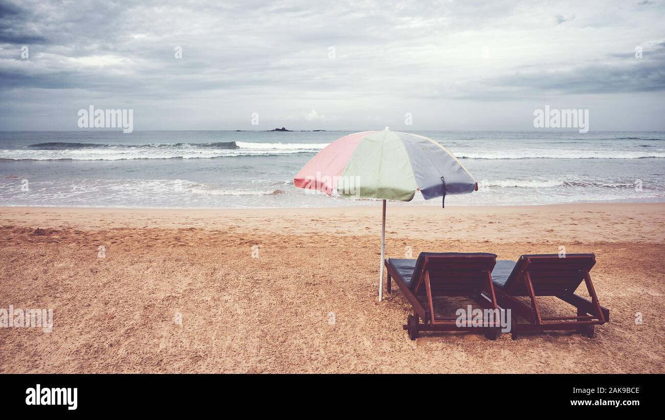 Two sunbeds and umbrella on an empty beach, color toning applied, Sri Lanka. Stock Photo