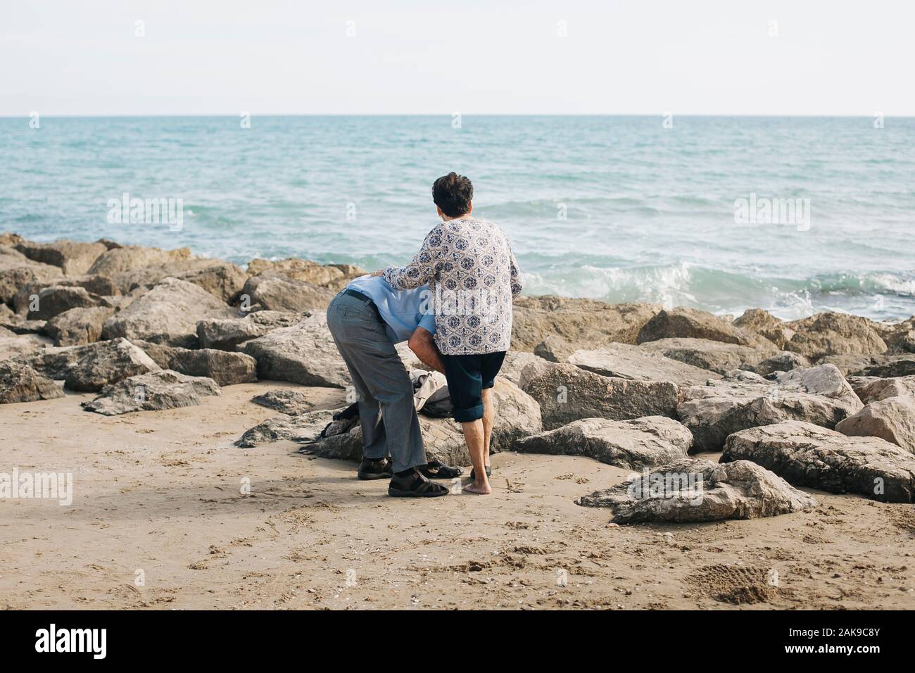 Elderly man helping his woman while walking on the beach. Vilanova i la Geltrú, Barcelona. Spain Stock Photo